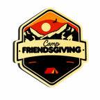 A hexagonal sticker or patch design featuring a mountain landscape with a red and orange sunset, black peaks, a white sun, a bird silhouette, and a cream banner reading 'Camp FRIENDSGIVING' across the center. A small red tent appears at the bottom.