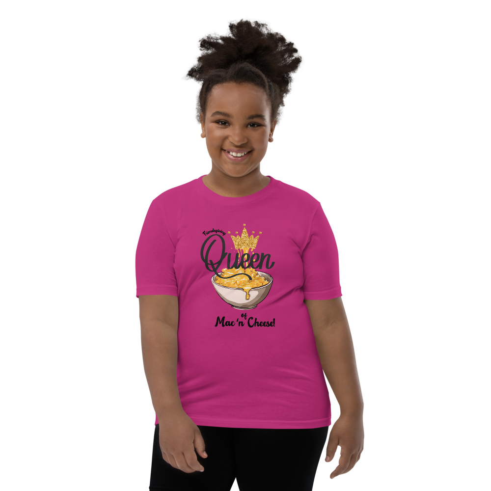 A smiling young girl with her hair in a high ponytail models a bright pink t-shirt. The t-shirt features a graphic of a bowl of cheese dip with a gold crown and the text 'Queen of by Mac 'n Cheese'.