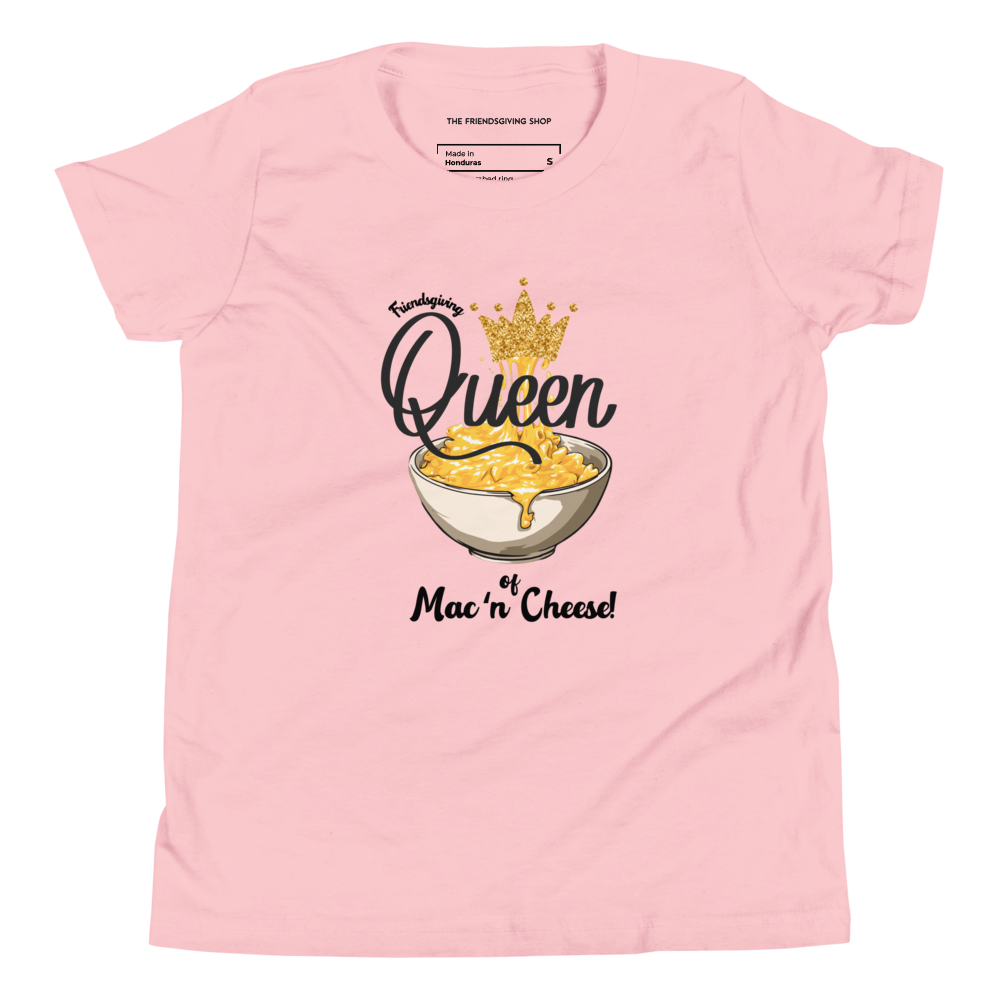 A light pink short-sleeve crewneck t-shirt featuring a graphic print of a bowl of cheese macaroni with a gold crown and the text 'Queen of Mac 'n Cheese!'. The inner collar label shows the brand 'The Frienddsgiving Shop'.