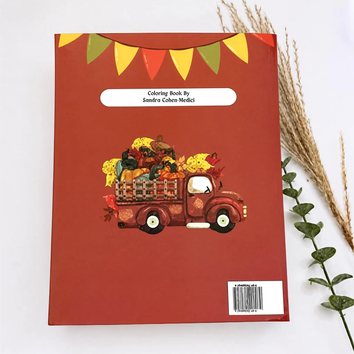 A hardcover book titled 'Another Book By Sandra Colton-Medici' with a red cover, featuring an illustration of a red pickup truck loaded with autumn pumpkins and flowers. The book is displayed flat on a white surface with decorative dried wheat and green leaves on the sides.