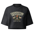 A dark charcoal gray cropped t-shirt featuring a vintage-style graphic on the front that reads 'FRIENDSGIVING UNIVERSITY' in cream lettering, with a brown teddy bear, a red and gold 'U' logo, and the phrase 'GATHER. FEAST.