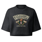 A dark charcoal gray cropped t-shirt featuring a vintage-style graphic on the front that reads 'FRIENDSGIVING UNIVERSITY' in cream lettering, with a brown teddy bear, a red and gold 'U' logo, and the phrase 'GATHER. FEAST.