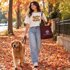 A woman walks a golden retriever on a leaf-covered autumn sidewalk while carrying a burgundy tote bag with a white logo that reads 'The Friendsgiving Shop' and 'Golden Hour Gravy' printed on her white graphic T-shirt.
