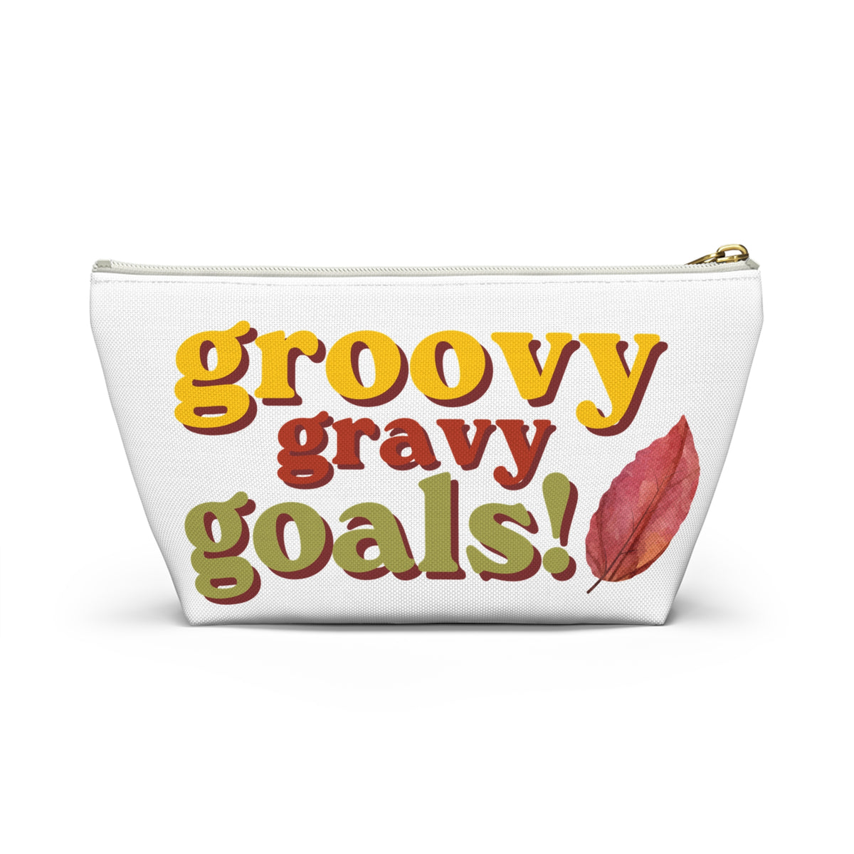 A white cosmetic pouch with a gold zipper, featuring the text 'groovy gravy goals!' in yellow, red, and green retro-style lettering, alongside a red autumn leaf graphic.