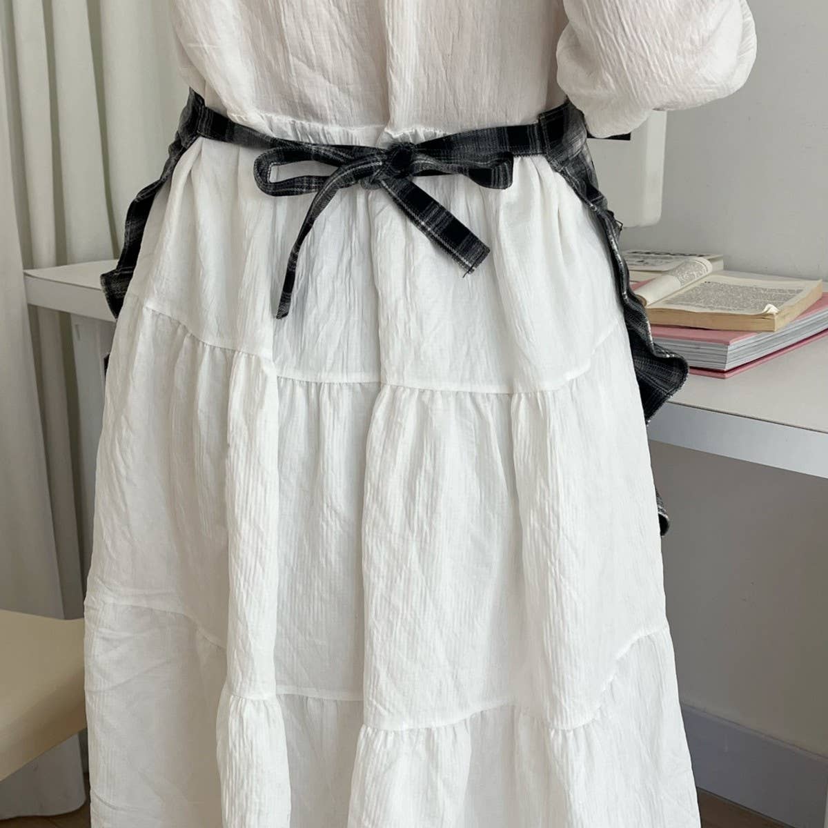 White dress with a black belt worn by a person, with a blurred indoor background.