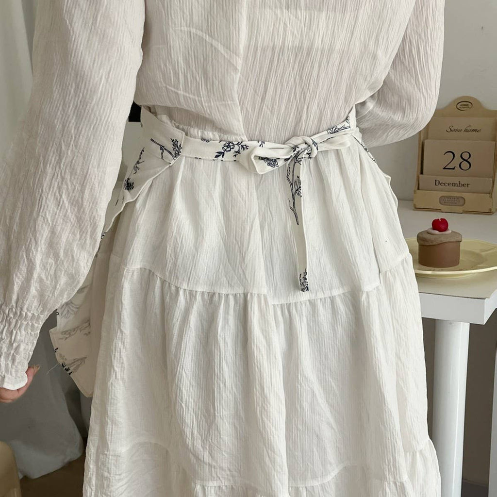 White dress with a floral belt worn by a person, with a blurred background.