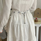 White dress with a floral belt worn by a person, with a blurred background.