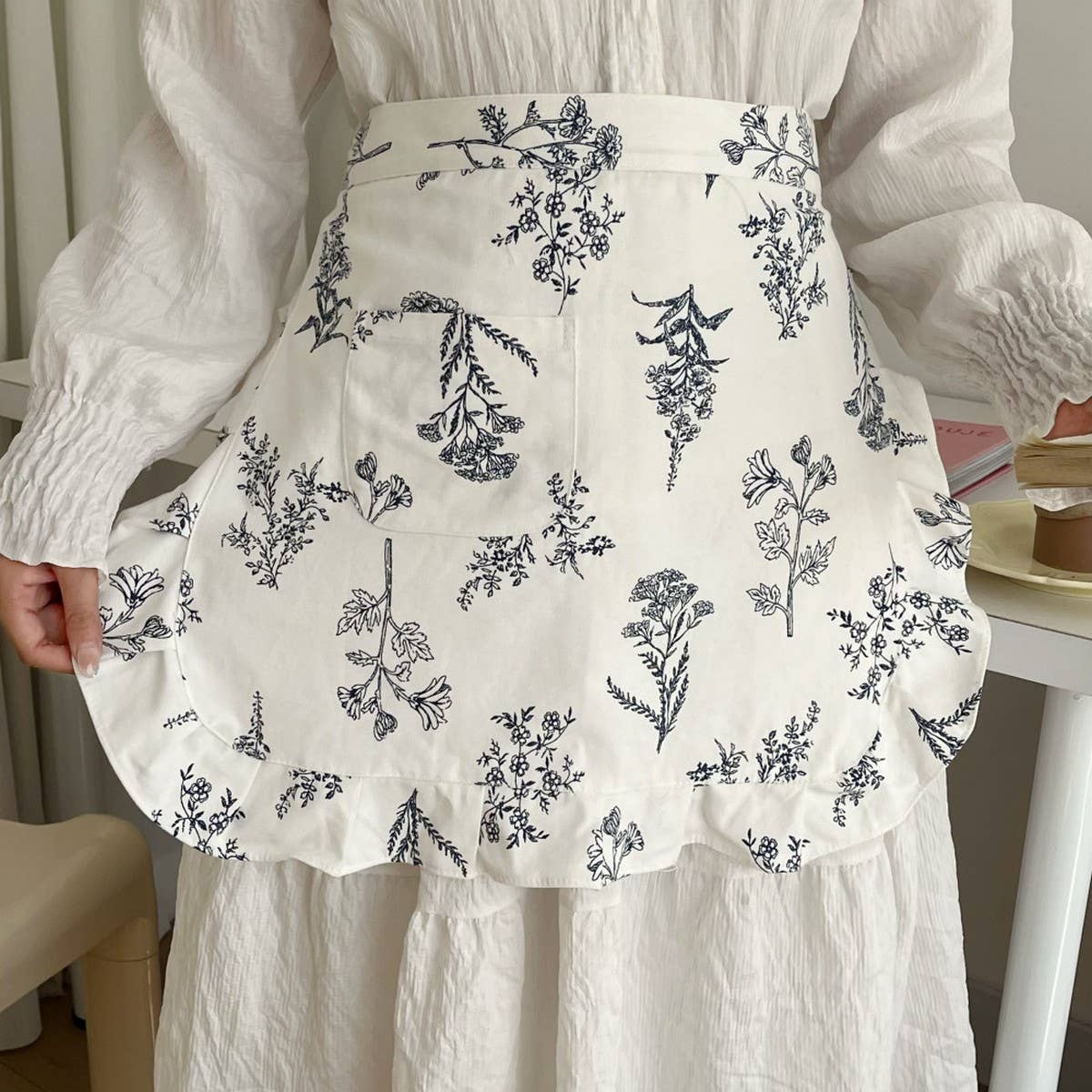 White apron with black floral pattern worn by a person, sitting on a chair.