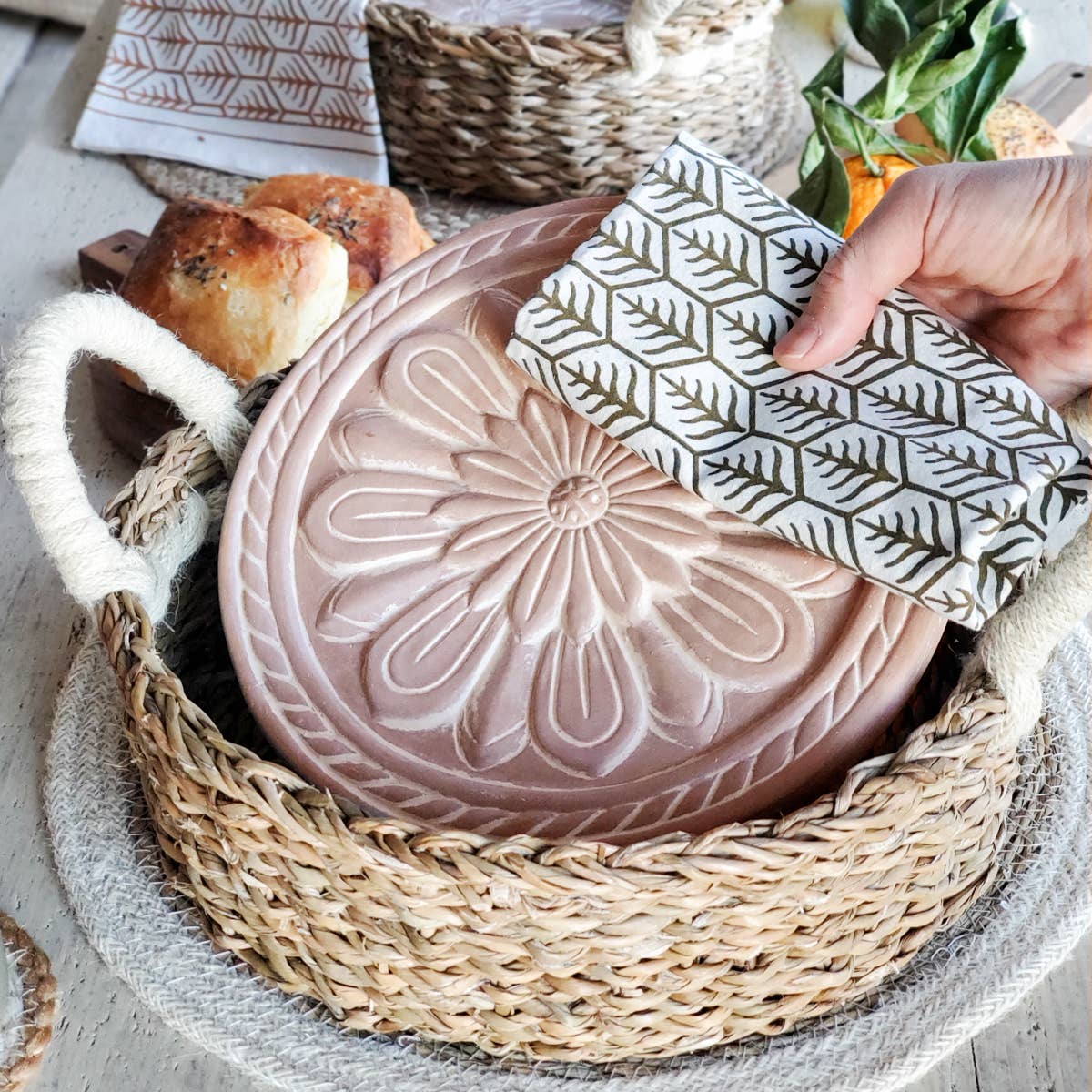 Decorative pink ceramic dish with embossed design in a woven basket, accompanied by a patterned napkin.