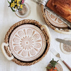Decorative plate with floral design in a woven basket on a table with bread and flowers.