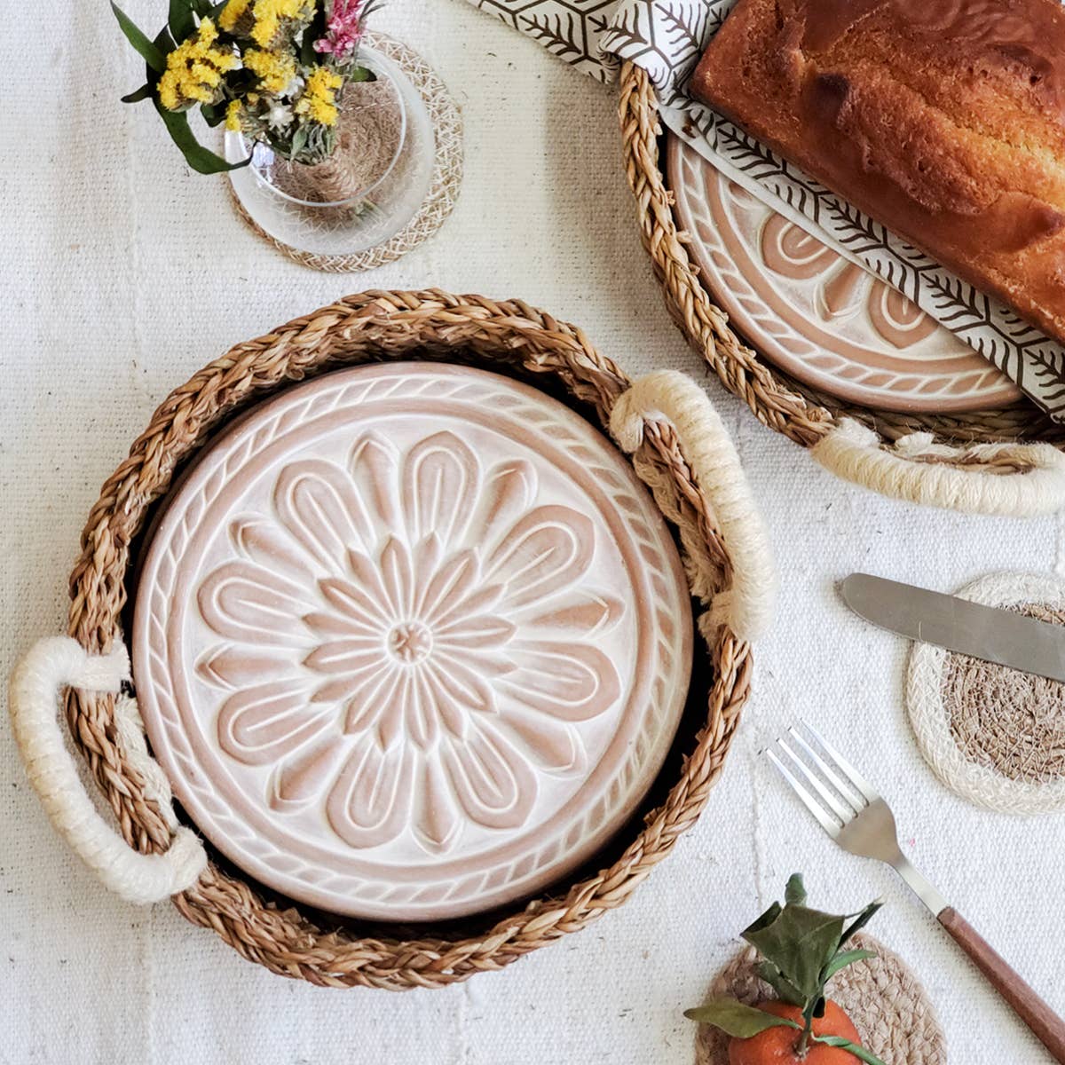 Decorative plate with floral design in a woven basket on a table with bread and flowers.
