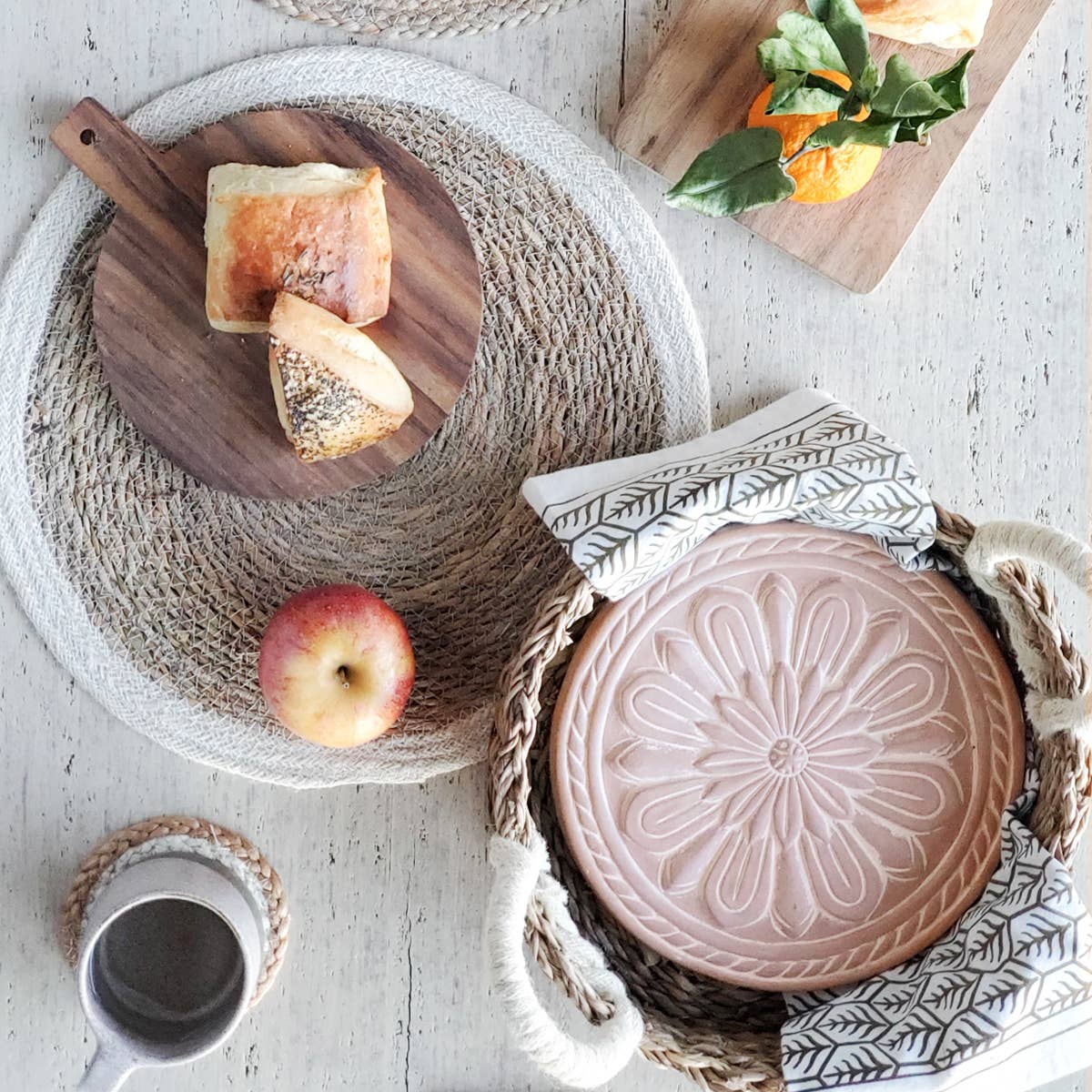 Round ceramic tray with embossed design on a textured surface with bread and an apple.