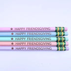 Five decorative pencils stacked horizontally on a light background. The pencils are pastel pink, light blue, and lavender, each printed with the text 'HAPPY FRIENDSGIVING' in dark brown next to a gold star.