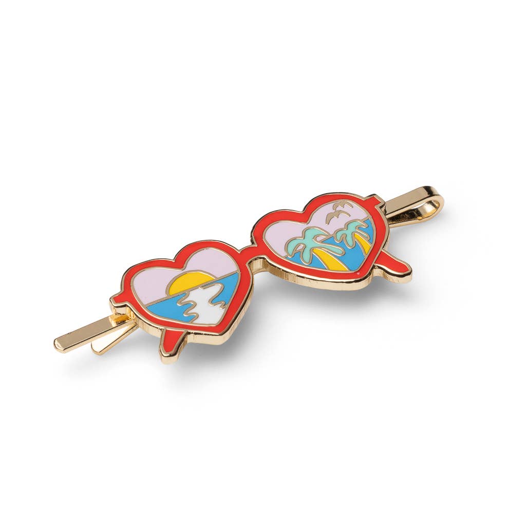 A pair of novelty heart-shaped sunglasses with gold-tone metal frames and colorful enamel details, featuring a beach sunset scene on one lens and palm trees on the other, set against a plain white background.
