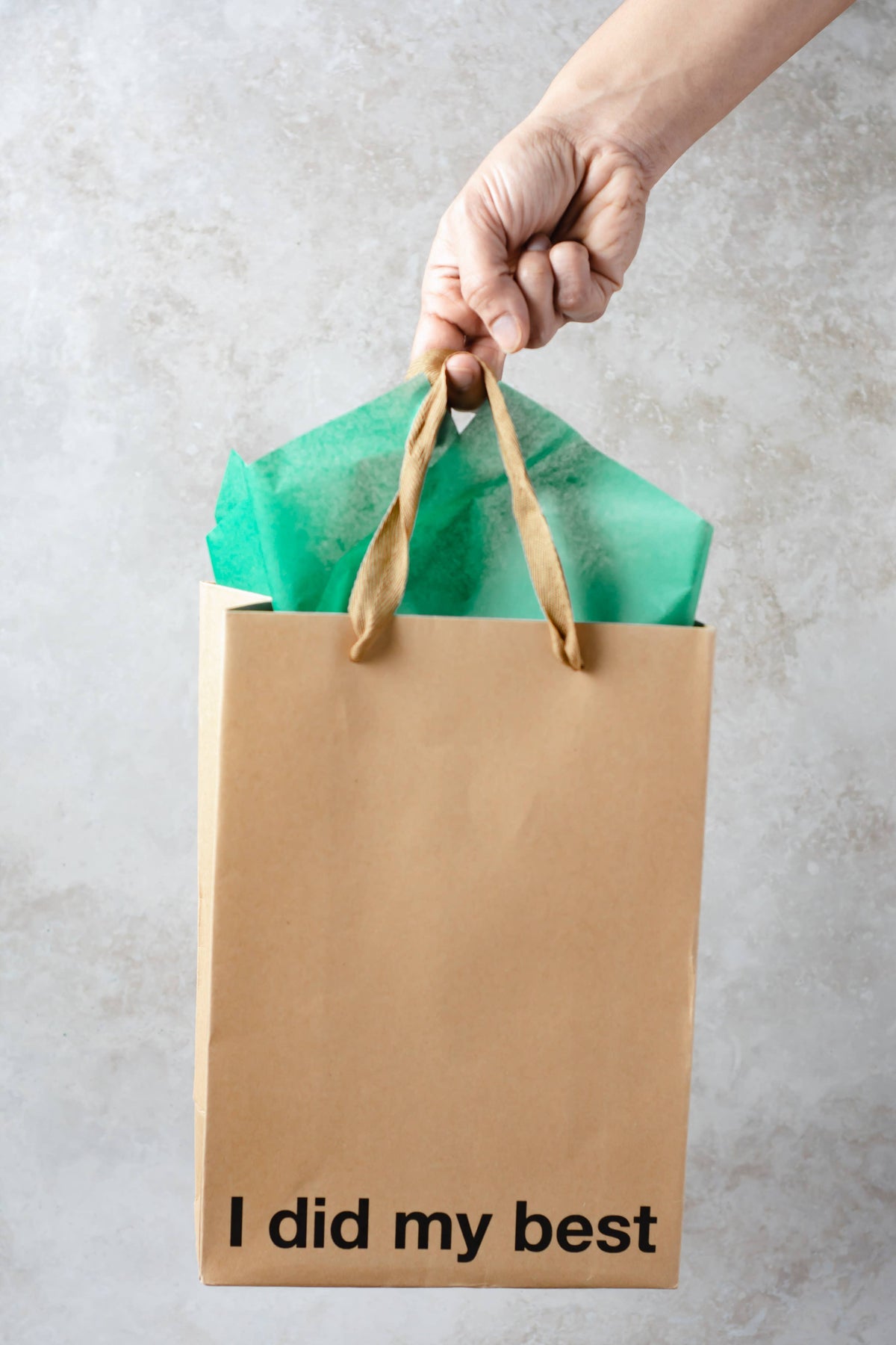 Hand holding a brown paper bag with 'I did my best' text against a light gray background