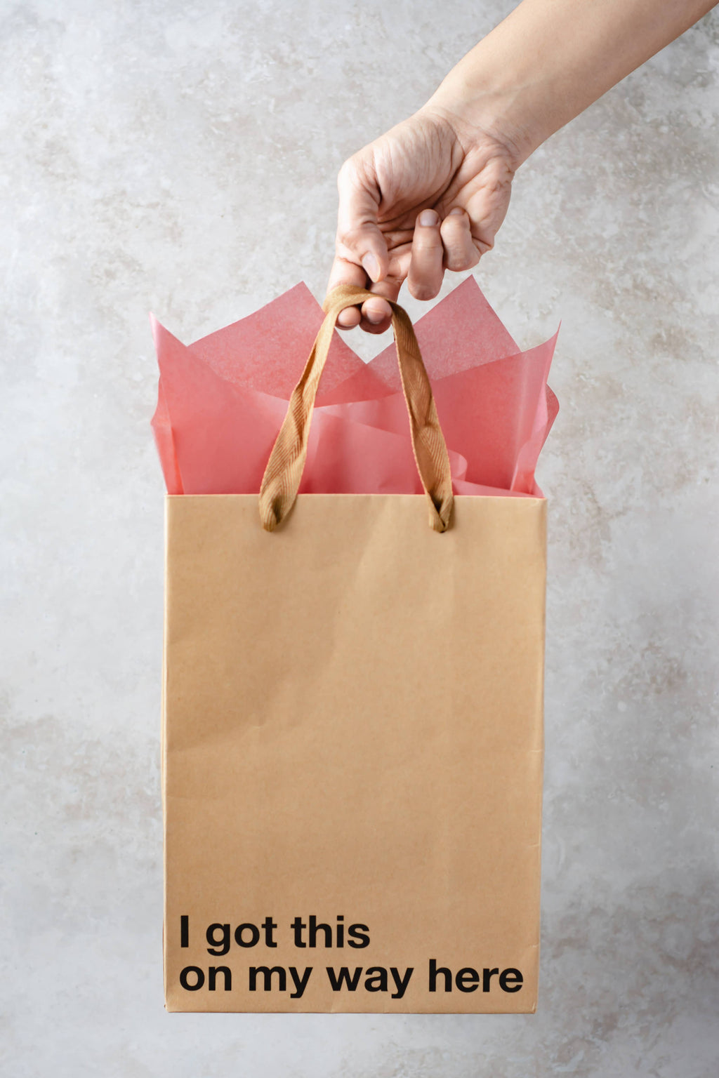 Brown paper bag with 'I got this on my way here' text held by a hand against a light background