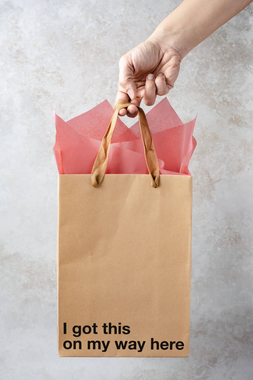 Brown paper bag with 'I got this on my way here' text held by a hand against a light background