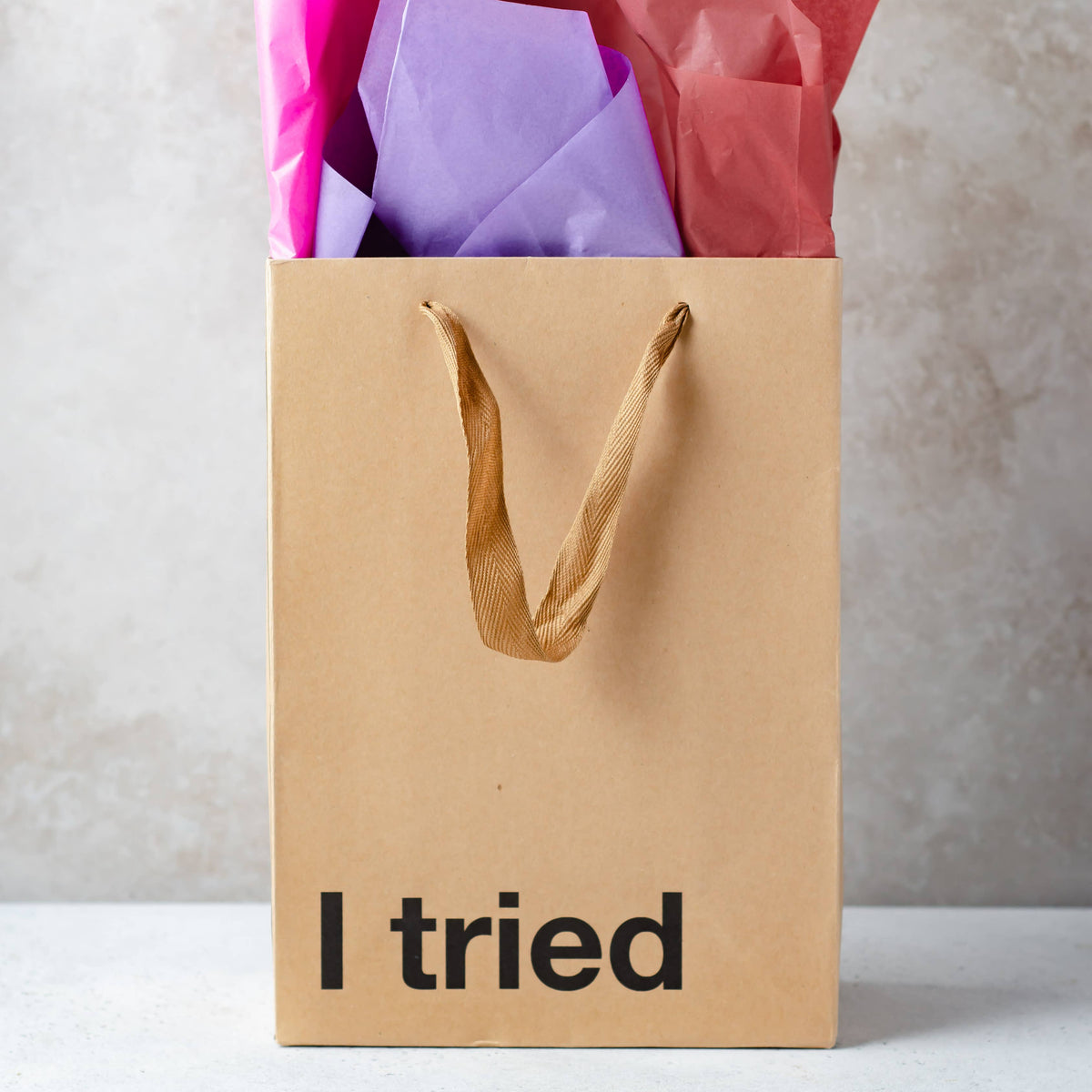 Brown paper bag with 'I tried' text, containing colorful tissue paper against a neutral background.