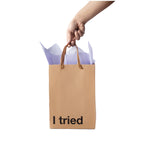 Kraft paper bag with 'I tried' text held by a hand on a white background