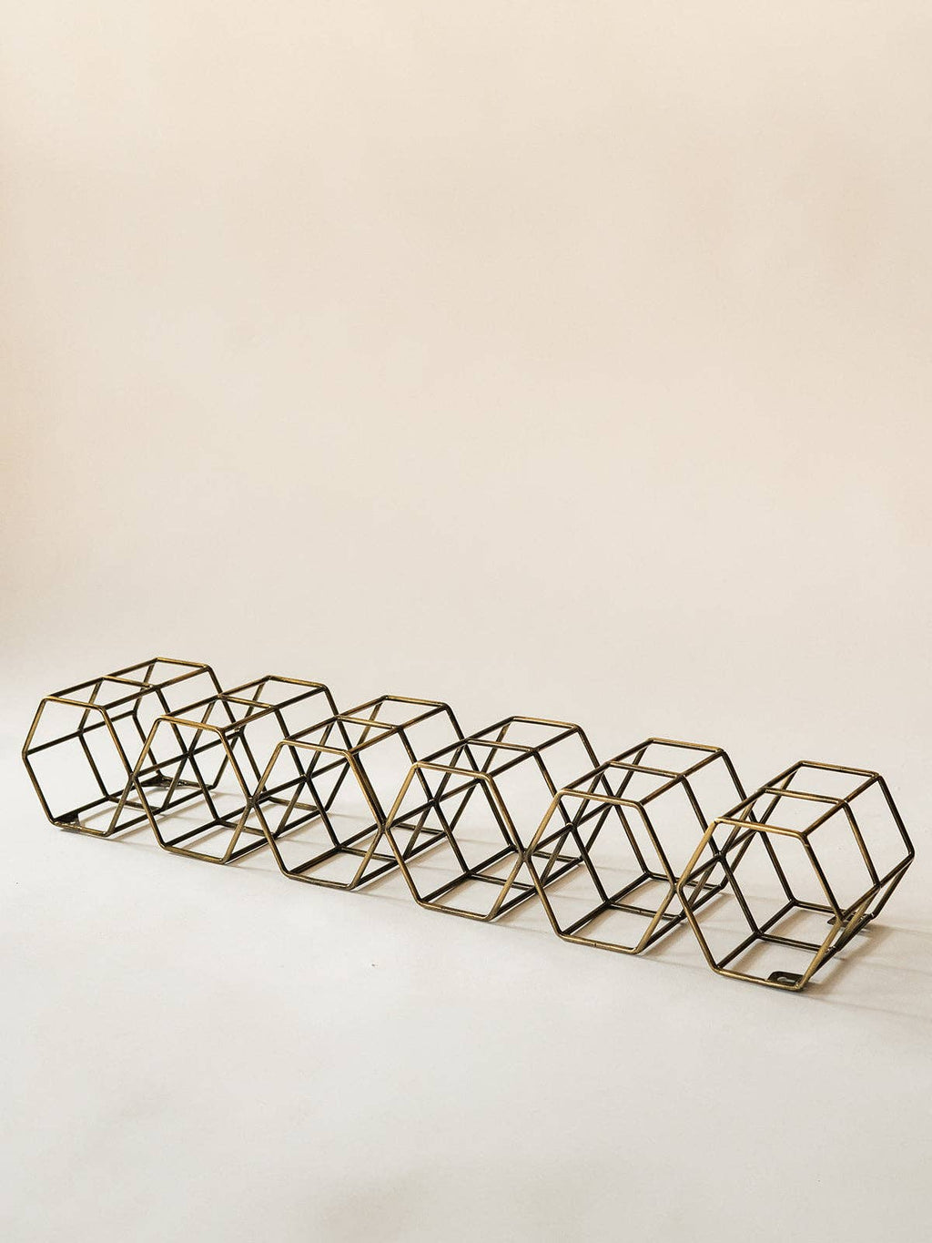 A set of six geometric wire cube candle holders in a bronze finish, arranged in a diagonal row on a plain off-white background.