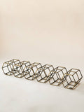 A set of six geometric wire cube candle holders in a bronze finish, arranged in a diagonal row on a plain off-white background.