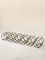 A set of six geometric wire cube candle holders in a bronze finish, arranged in a diagonal row on a plain off-white background.