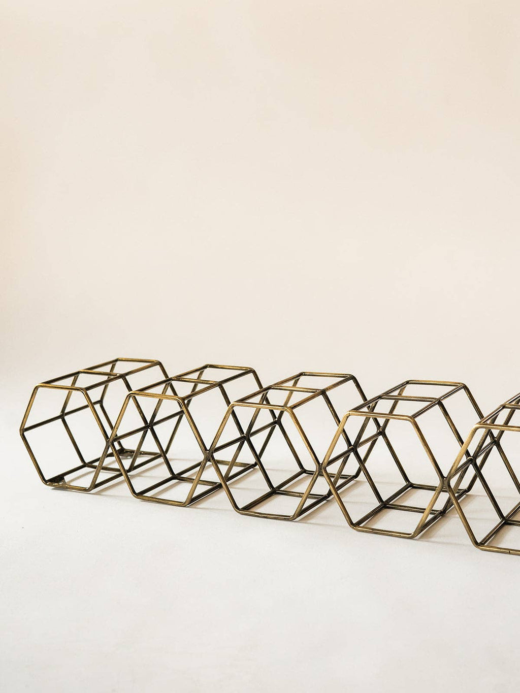 A row of geometric wire cube planters in a gold finish, arranged diagonally on a light beige background.