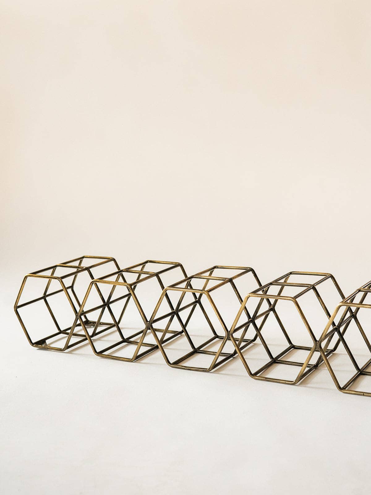 A row of geometric wire cube planters in a gold finish, arranged diagonally on a light beige background.