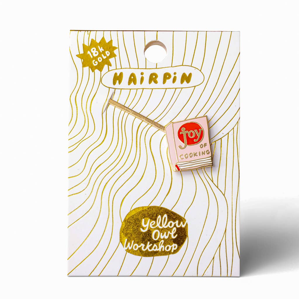 A 18k gold hairpin enamel pin displayed on its branded backing card. The pin is shaped like a matchbook with a red circular logo reading 'joy of COOKING' and a gold matchstick.