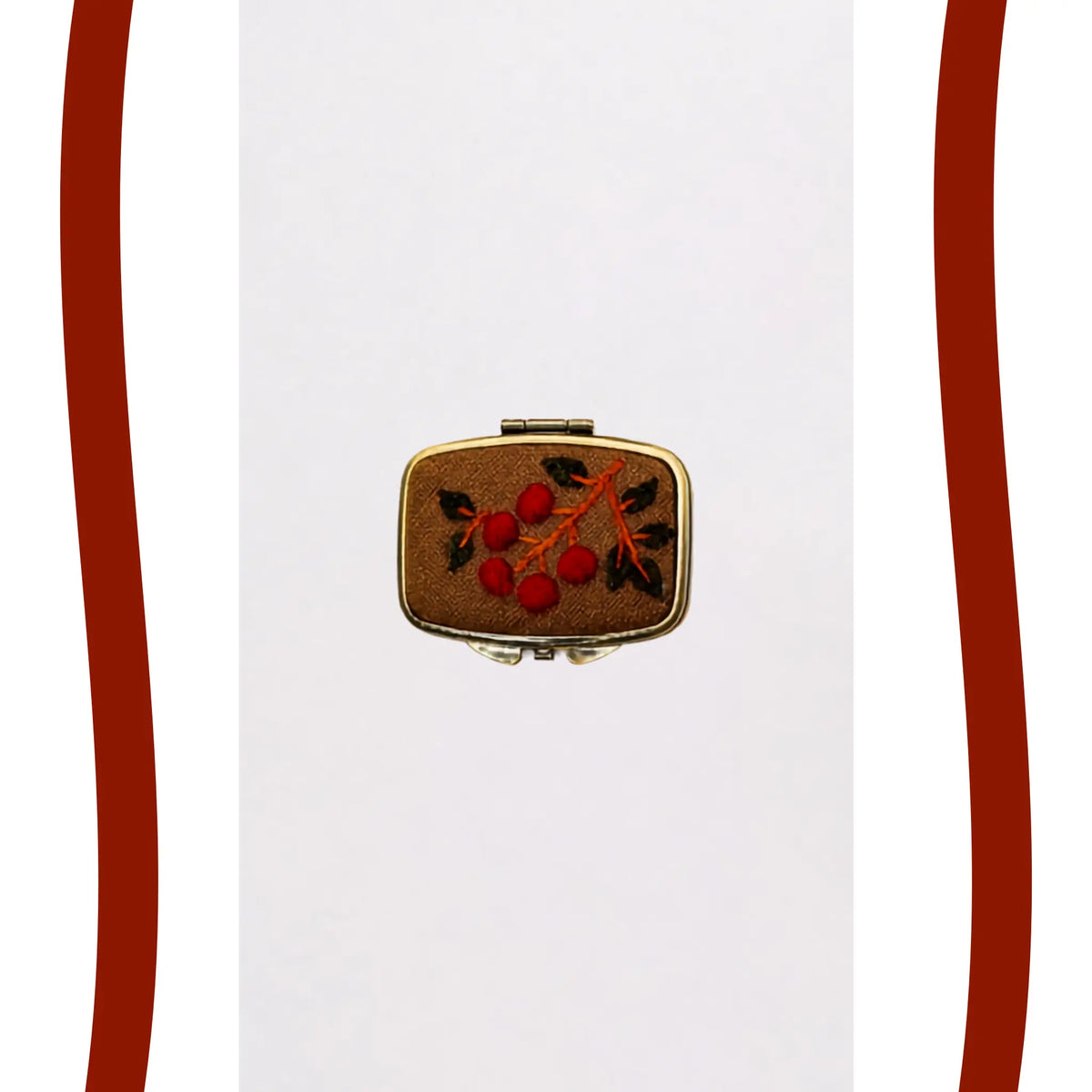 A small rectangular gold-toned case or box with a brown textured cover, decorated with an embroidered or painted red berry motif and dark green leaves, centered on a white background with decorative red side bars.