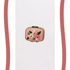A small rectangular pink clutch or compact case with gold-tone metal edges and an embroidered floral design featuring pink, white, and green flowers on a plain white background.