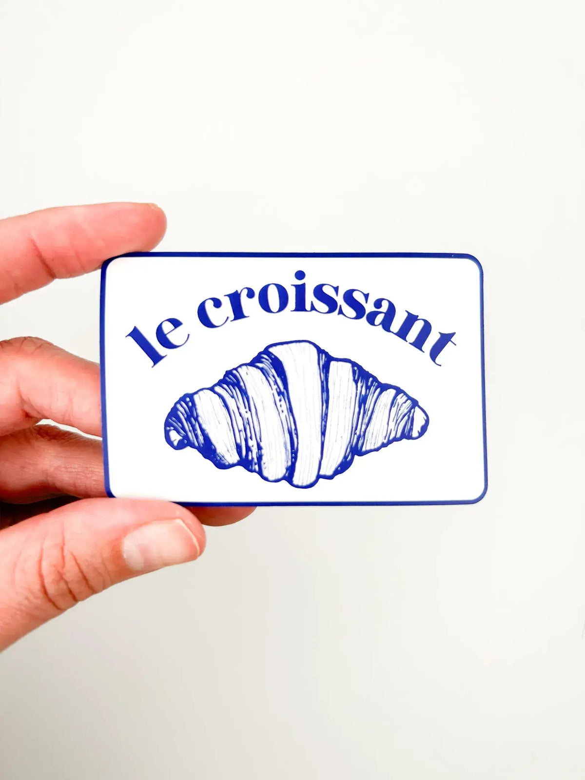 Card with a croissant illustration and 'le croissant' text held by a hand against a white background