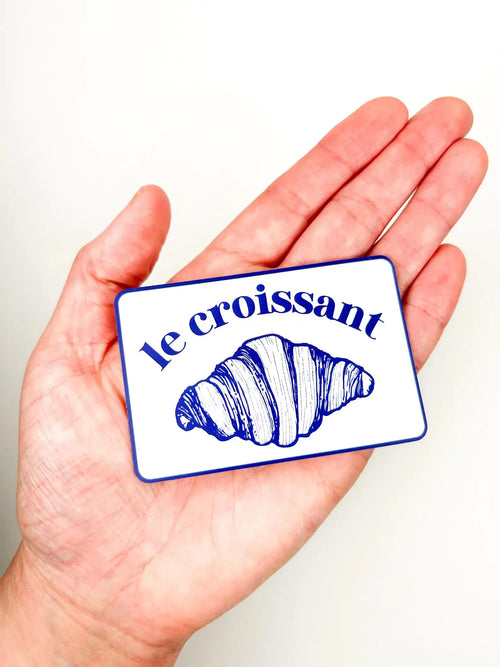 Hand holding a card with 'le croissant' and a croissant illustration on a white background