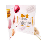 A folded greeting card featuring colorful macarons and a yellow bow illustration, with a handwritten message that reads, 'Life is better with a group of friends and a box of macarons. So glad you're in my Permanent Six
