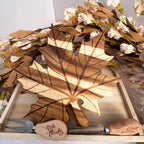 A wooden leaf-shaped serving board or tray insert with engraved leaf veins, displayed in a wooden tray with a small wooden-handled fork engraved 'Give Thanks' and a small wooden-handled utensil engraved 'Thank You'. Decorative dried flowers and leaves surround the tray.