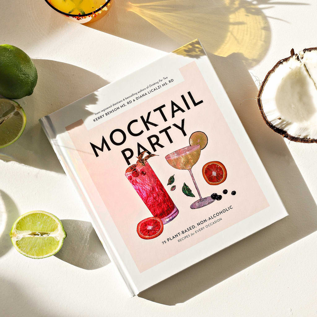 Book titled 'Mocktail Party' with cocktail illustrations on a light surface with limes and a coconut.