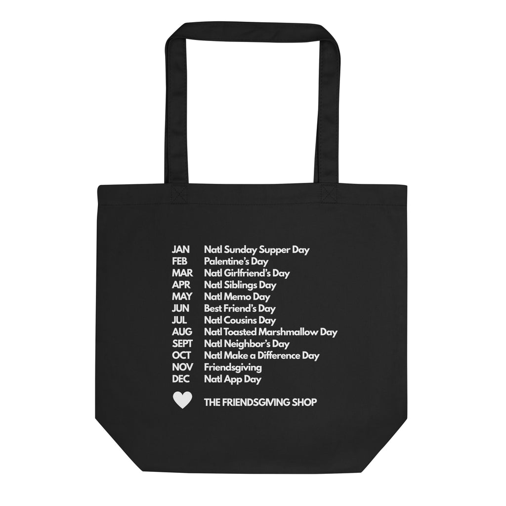 A black canvas tote bag with two handles, featuring a white printed list of 'Noot' days around the calendar and the text 'THE FRIENDSGIVING SHOP' with a small heart at the bottom.