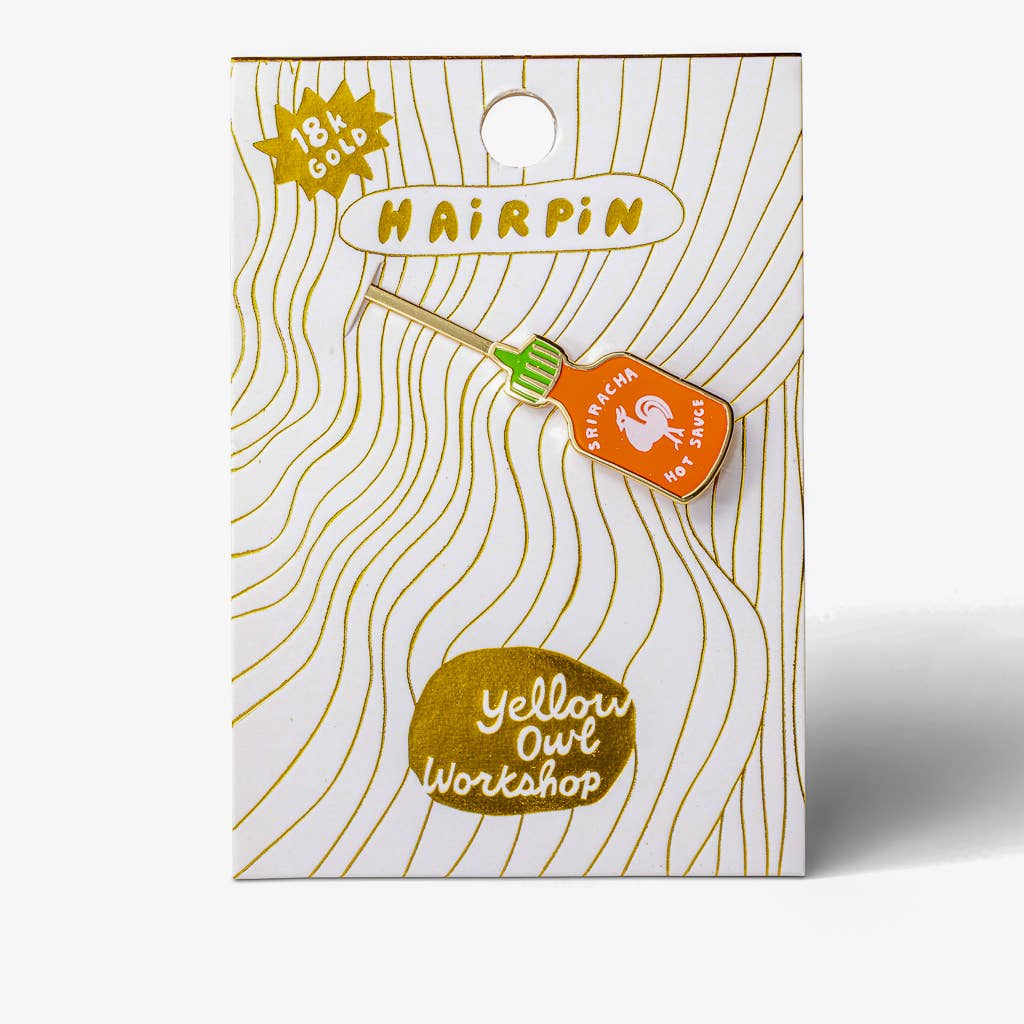 An enamel pin shaped like a hot sauce bottle, displayed on its branded backing card. The pin features an orange body with a white ghost logo and the words 'SIRACHA HOT SAUCE', a light wood-toned handle, and a green cap.