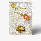 An enamel pin shaped like a hot sauce bottle, displayed on its branded backing card. The pin features an orange body with a white ghost logo and the words 'SIRACHA HOT SAUCE', a light wood-toned handle, and a green cap.