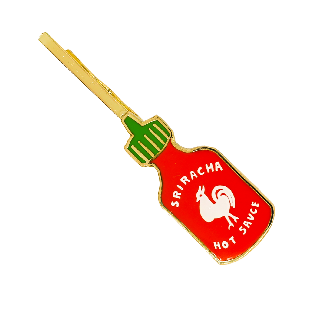 A Sriracha hot sauce bottle-shaped hair clip with red, green, white, and gold enamel details, shown on a plain white background.