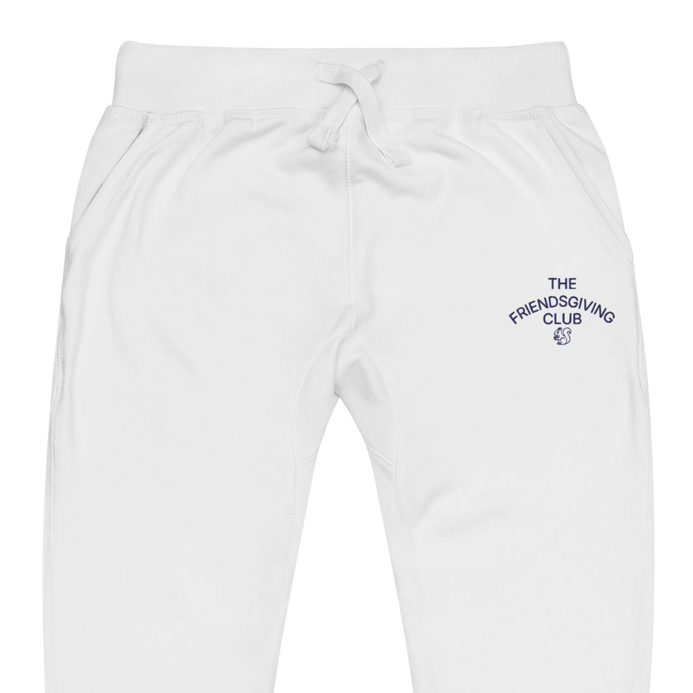 White sweatpants with a drawstring waist and a small navy blue graphic embroidered on the left thigh that reads 'THE FRIENDS GIVING CLUB'.