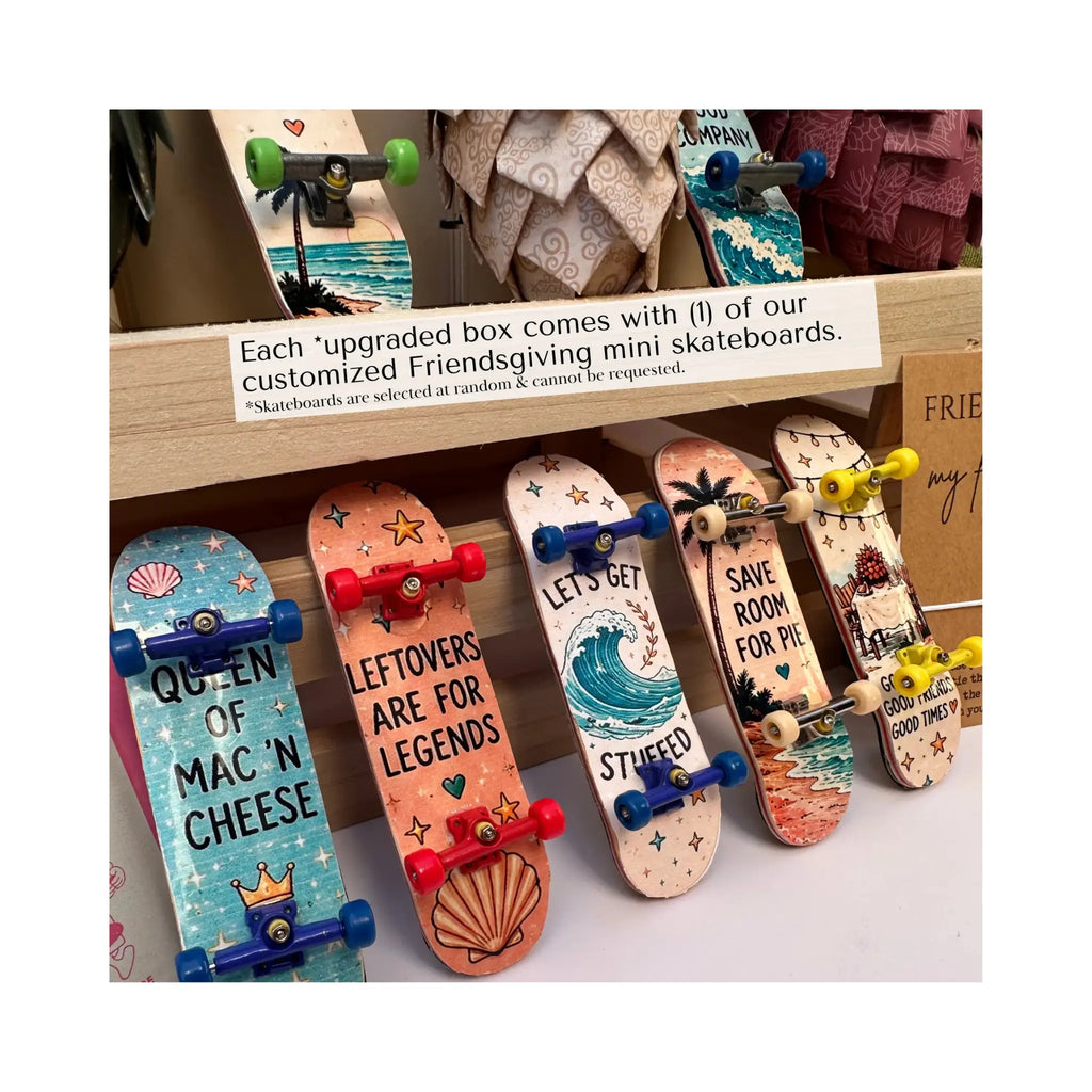 A display of mini skateboard gift boxes with colorful printed skateboards featuring custom designs and quotes, arranged on a wooden shelf with a sign explaining the customization process.