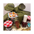 A gift basket arrangement featuring an olive green burlap ribbon bow, a silver tin with autumn leaf artwork, jars with red-and-white gingham lids, a vintage-style candy tin, and a bottle of burgundy nail polish on a light neutral background.
