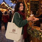 A woman at a festive outdoor hot cocoa stall carries a cream canvas tote bag with a brown logo that reads 'THE FRIENDSGIVING SHOP'. She is wearing a green sweater and a burgundy scarf, smiling as she receives a hot cocoa cup from a vendor.