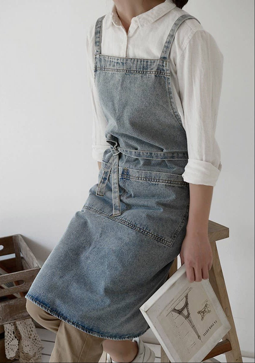 Person wearing a denim apron holding a book in a minimalistic setting