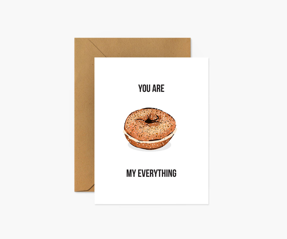 A white greeting card with a brown bagel illustration and the text 'YOU ARE MY EVERYTHING', shown with a brown kraft envelope on a light gray background.