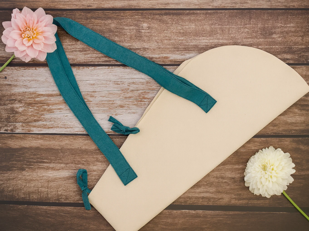 Beige makeup bag with teal strap on a wooden surface with flowers.