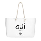 A white canvas tote bag with cream-colored rope handles, featuring the word 'oui' in black script and a small graphic with the text 'THE FRIENDSGIVING SHOP' printed on the front.